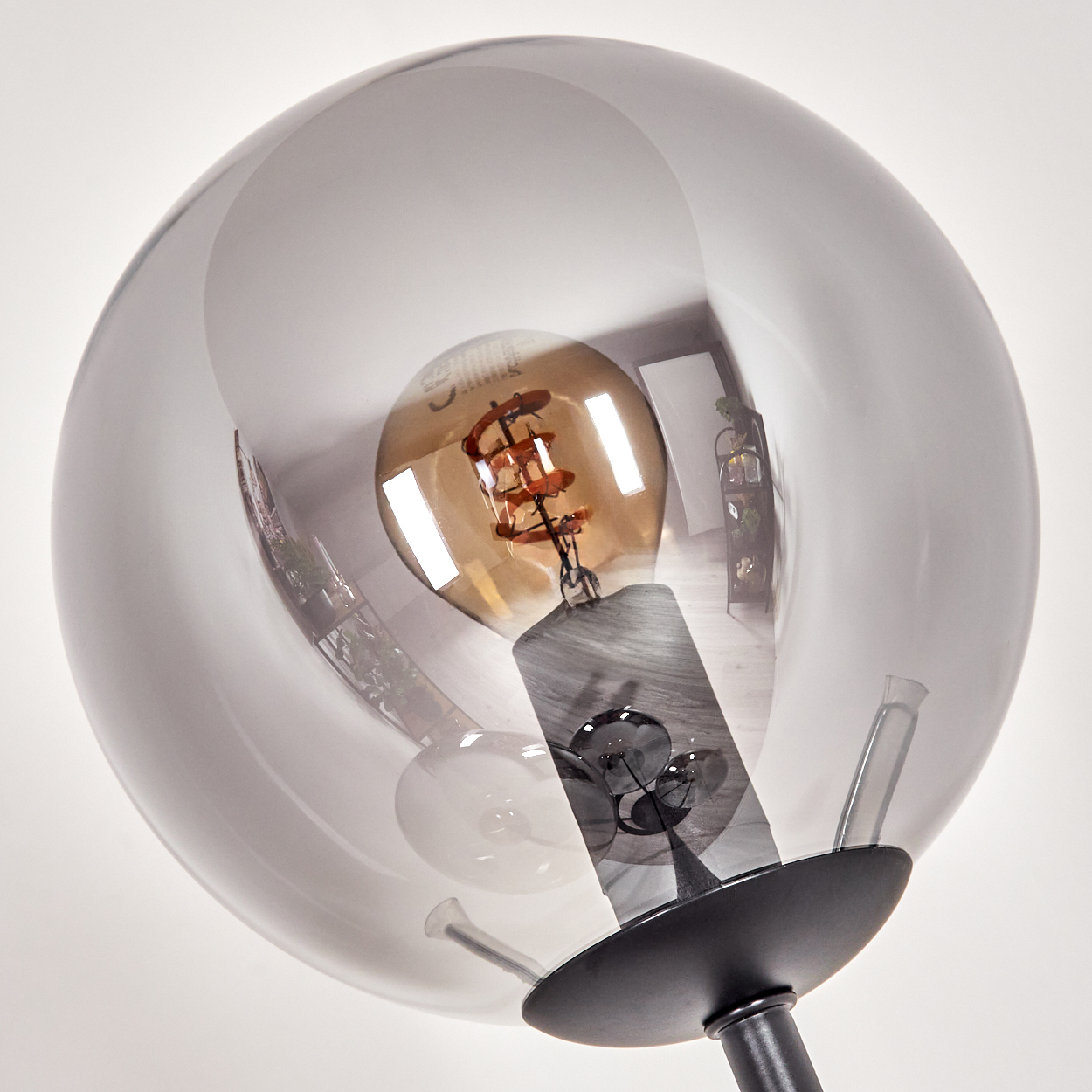 Nahaufnahme einer modernen Lampe. Eine klare Glaskugel umgibt eine warm getönte Glühbirne. Der Sockel ist schwarz, der Hintergrund weiß.