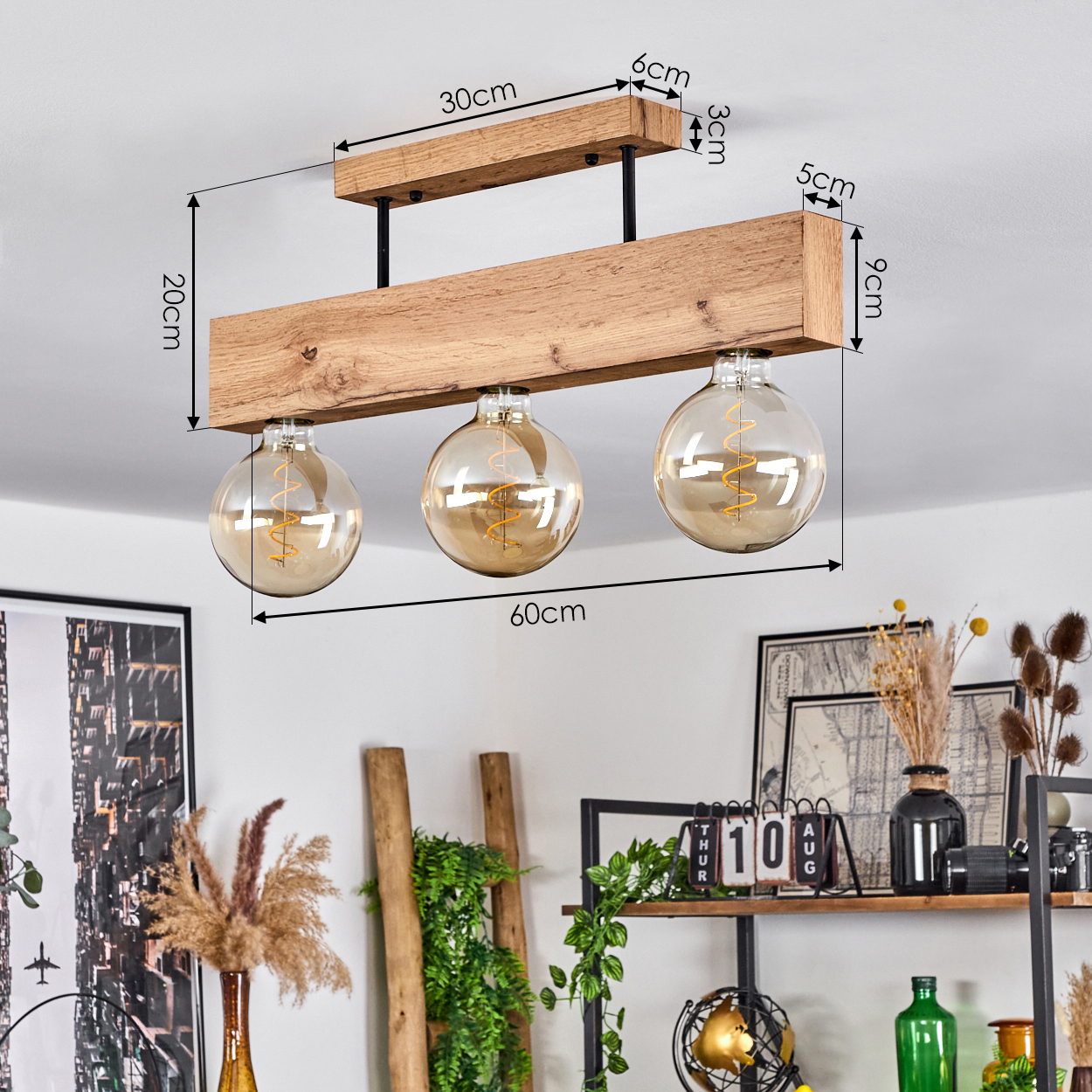 Hölzerne Deckenlampe mit drei Glühbirnen. Im Hintergrund ist ein Raum mit Dekoration, Pflanzen und einem Kalender zu sehen.