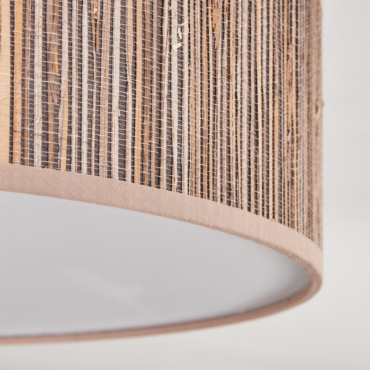 Nahaufnahme eines Lampenschirms mit gewebter, braun-beiger Struktur und weißem Innenraum. Beige Stoffverkleidung am Boden.