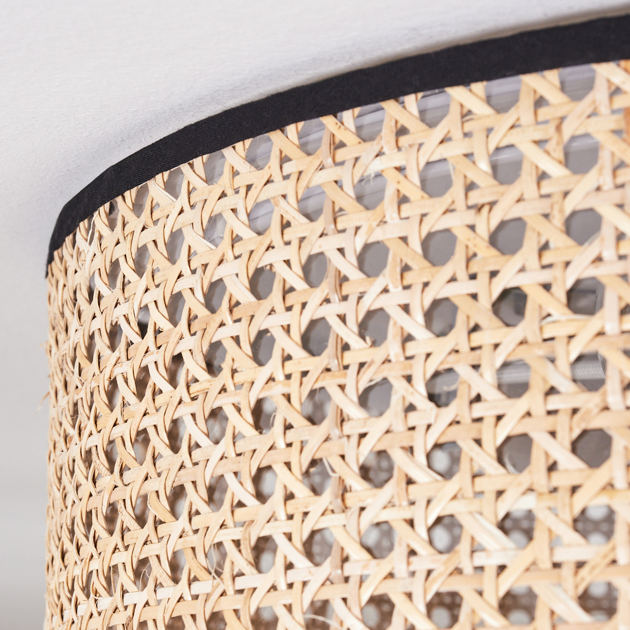 Nahaufnahme eines Lampenschirms aus geflochtenem Rattan mit schwarzem Rand. Das Geflecht erzeugt ein Muster aus rautenförmigen Löchern.