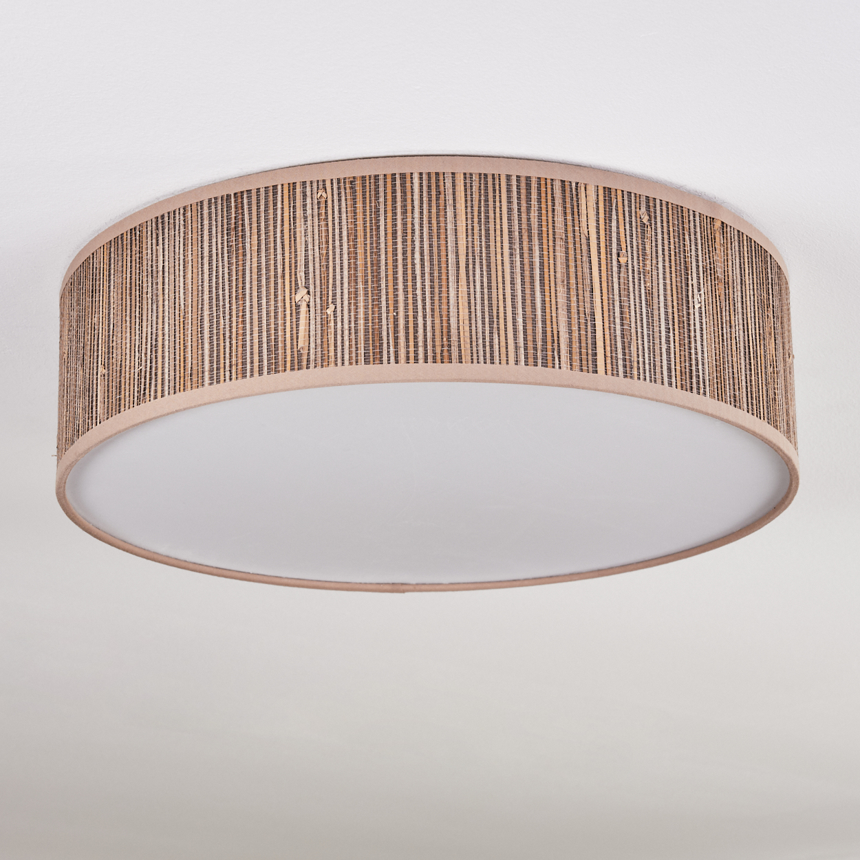 Eine runde Deckenlampe mit gewebtem Bambusschatten und weißem Diffusor, vor schlichtem, weißem Hintergrund.
