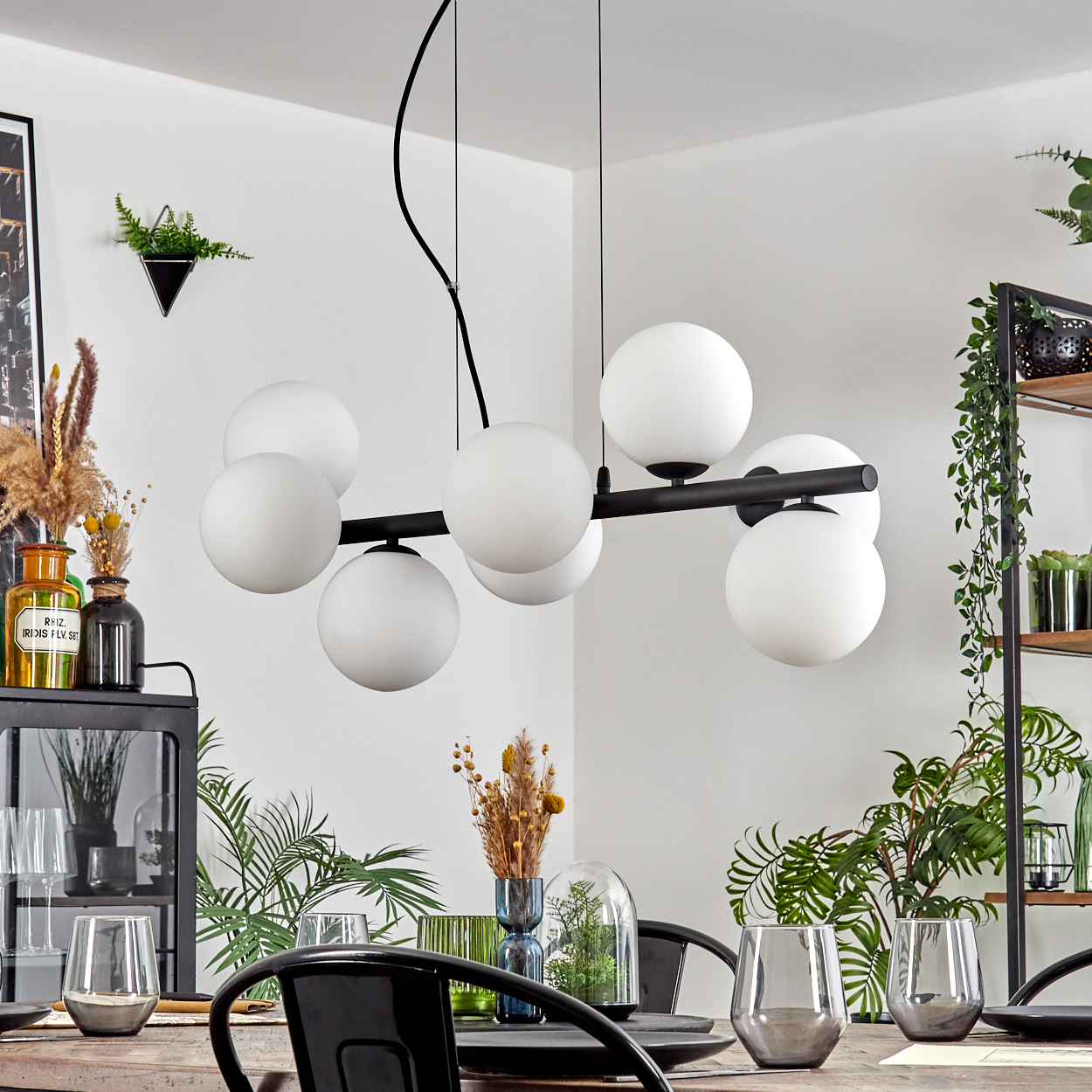 Esszimmer mit schwarzem Kronleuchter mit weißen Kugeln. Tisch mit Gläsern und Pflanzen gedeckt.