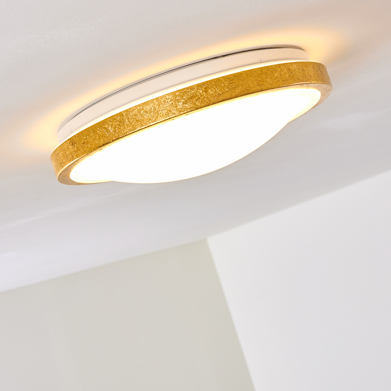 Eine moderne Deckenleuchte mit goldfarbenem strukturiertem Rand. Sie hat eine weiße Mitte und ist an einer weißen Decke befestigt.
