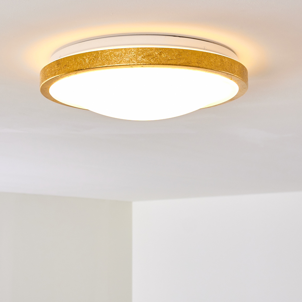 Eine moderne, runde Deckenleuchte mit goldenem Rand und hellem, weißem Licht. Decke und Wände sind weiß.