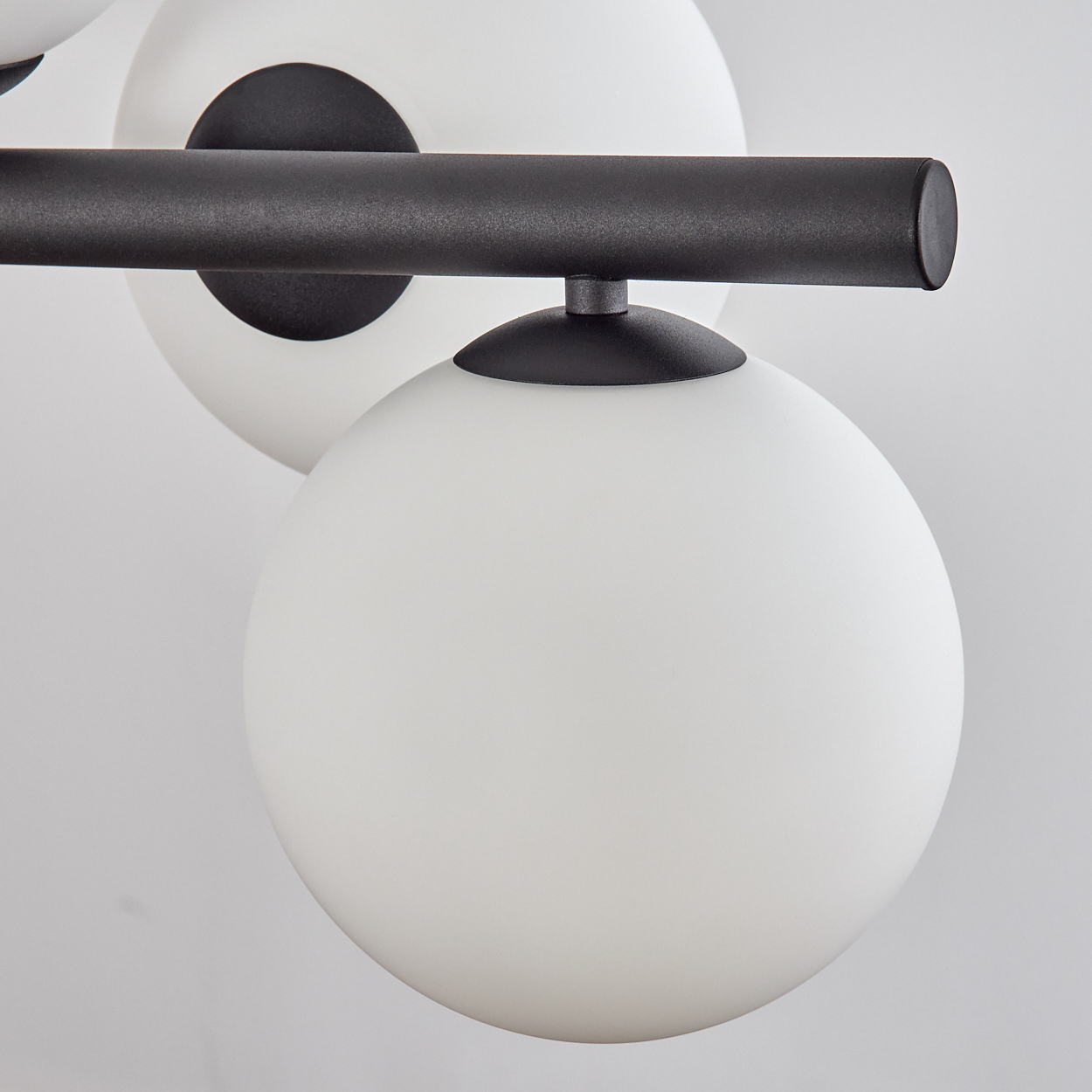 Nahaufnahme einer Leuchte mit weißen kugelförmigen Lichtern und schwarzen Metallstangen vor weißem Hintergrund.