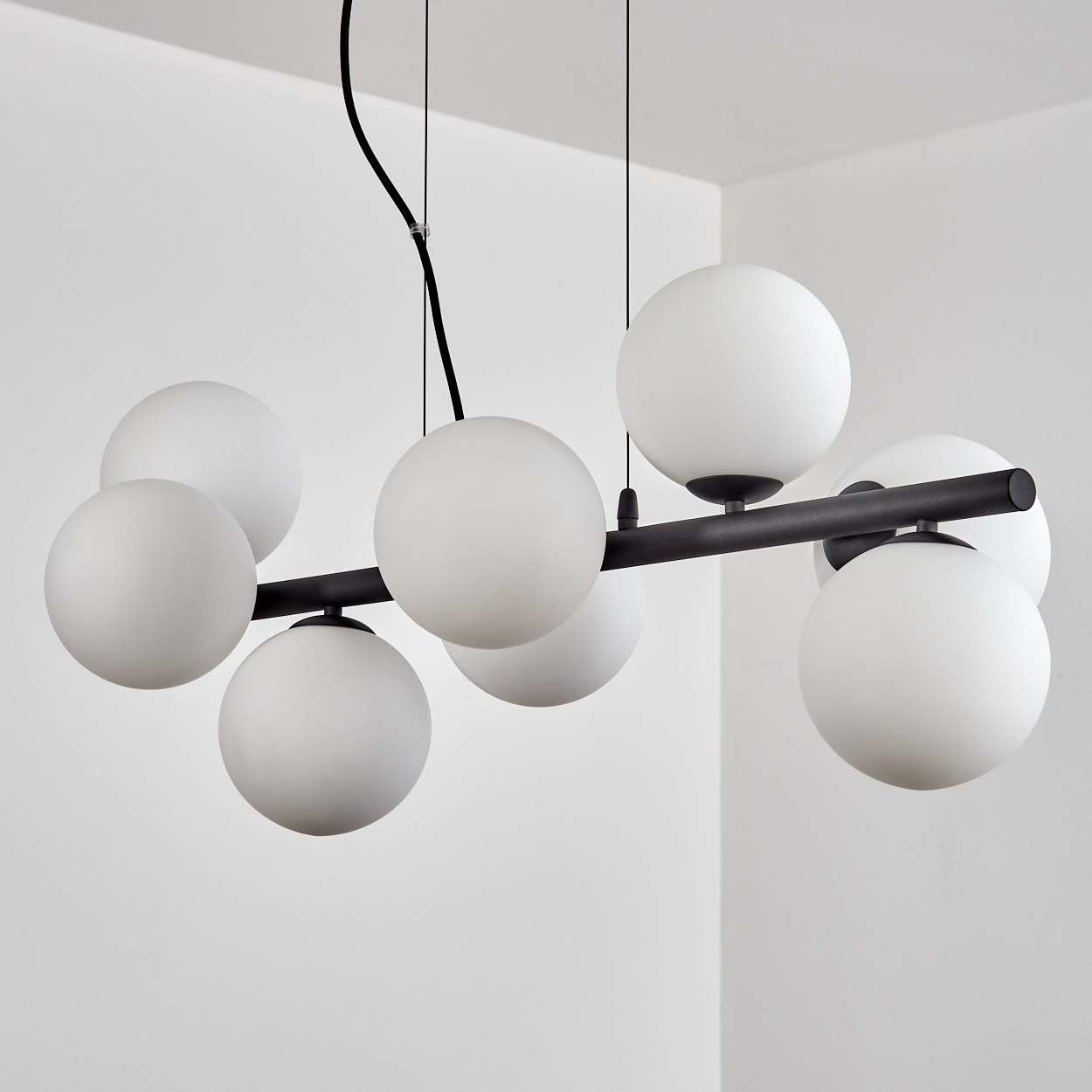 Eine moderne Hängelampe mit weißen Kugeln. Schwarze Stangen tragen die Kugeln. Der Hintergrund ist eine weiße Wand.