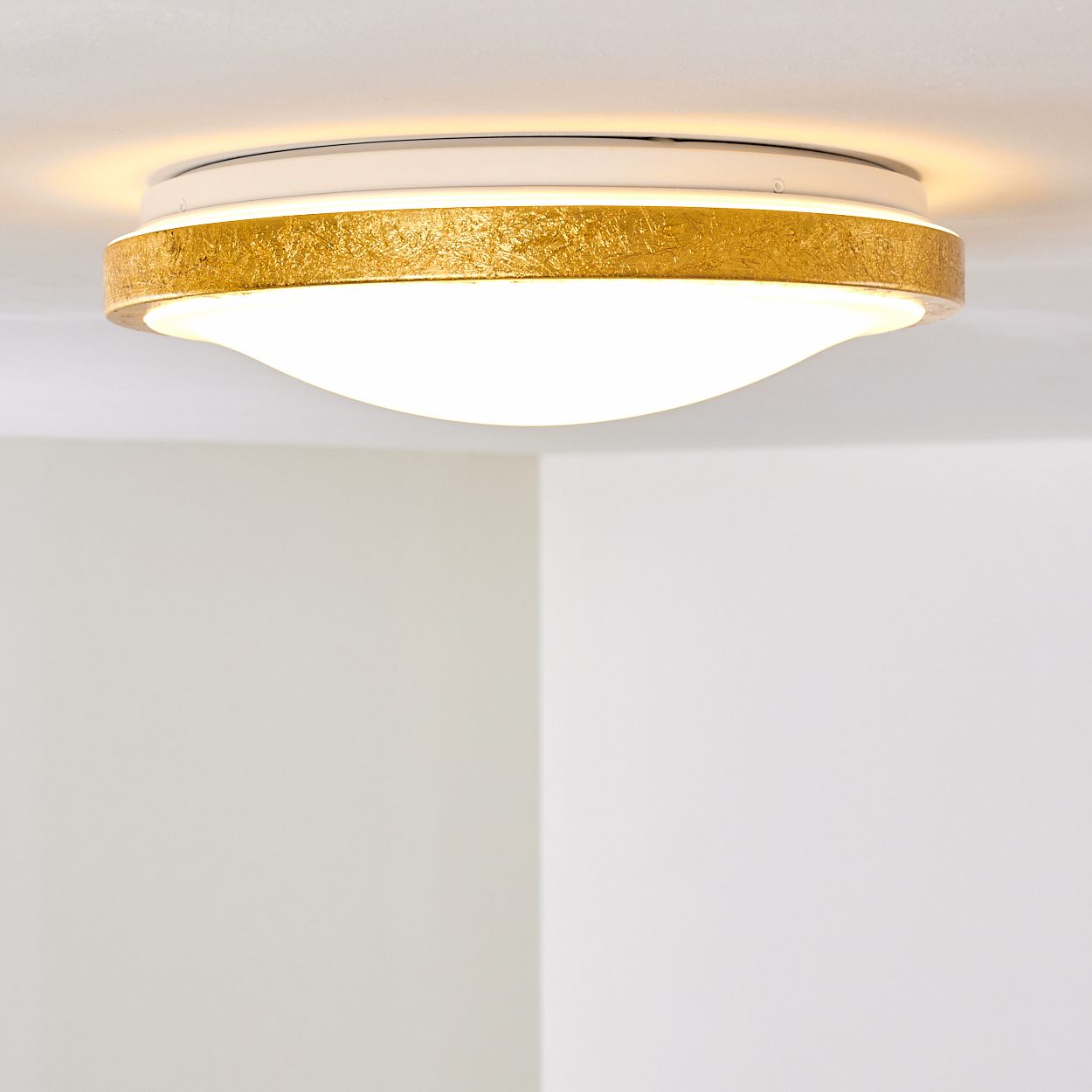 Eine moderne Deckenleuchte mit einem gold strukturierten Band und einem weißen, geschwungenen Lichtdiffusor. Der Hintergrund ist eine weiße Decke.