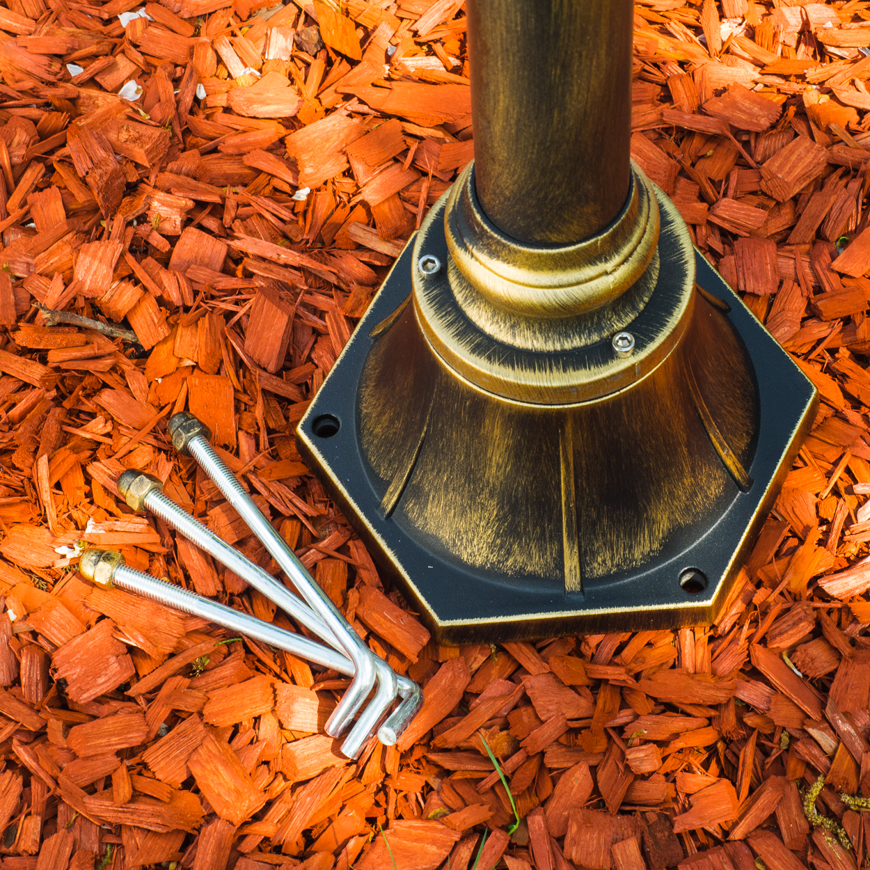 Ein bronzefarbener Lampensockel und -mast auf roter Mulch. Schrauben und ein Inbusschlüssel liegen verstreut herum.