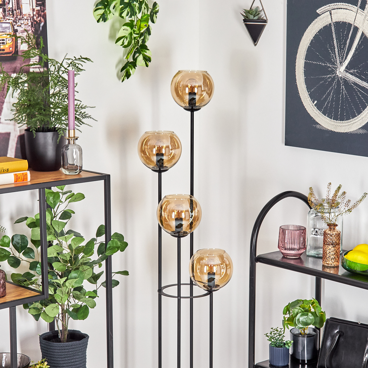 Ein Raum mit dekorativen Objekten. Eine Lampe mit vier bernsteinfarbenen Glaskugeln, Pflanzen und Regalen mit anderen Dekorationsartikeln.