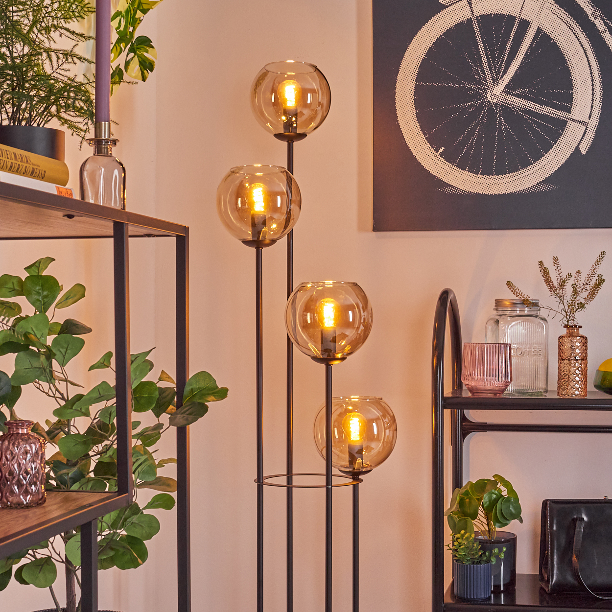 Eine moderne Stehlampe mit vier Glaskugeln, Bücherregalen, einem Fahrradrad-Druck und verschiedenen dekorativen Gegenständen.