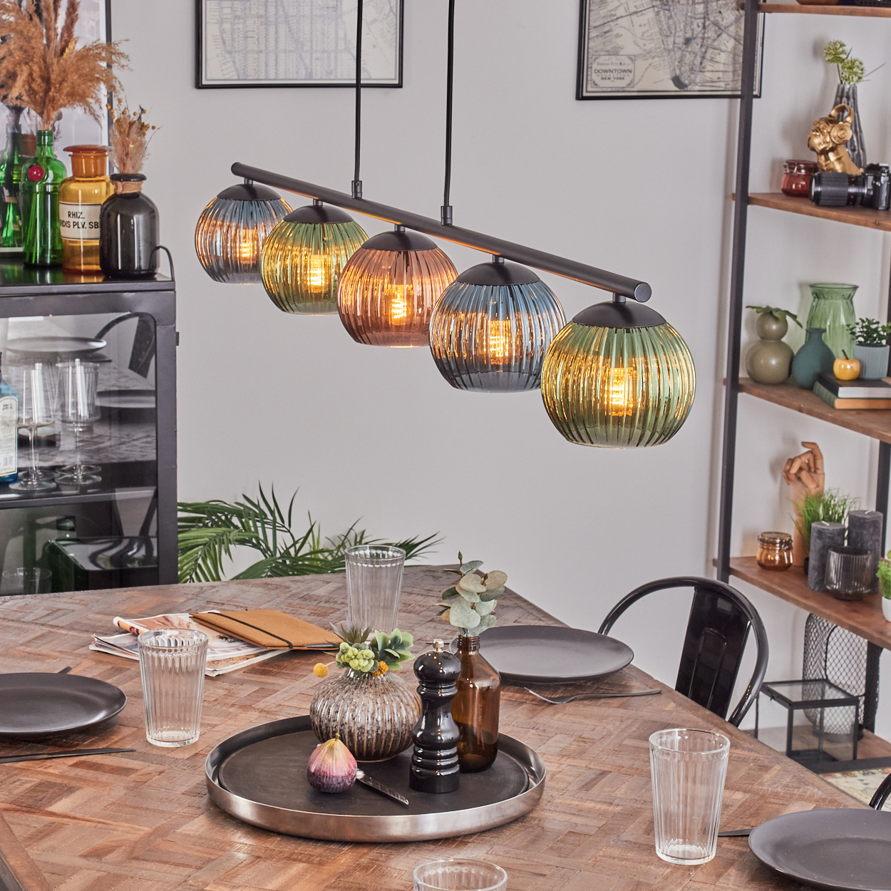 Esszimmer mit Holztisch, Hängelampen und Tischdeko. Regale mit Deko und Glasartikeln an der Seite.