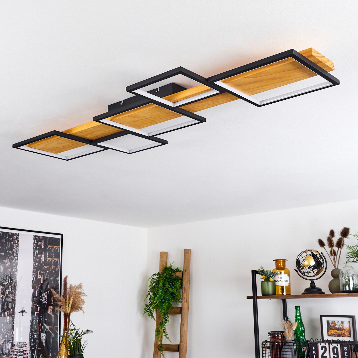 Moderne Deckenleuchte mit Holz- und schwarzen Quadratrahmen. Eine Holzleiter und ein Regal mit Dekoration darunter.