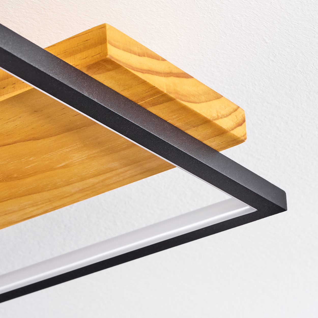 Nahaufnahme eines Holzregals und einer schwarz gerahmten Leuchte vor einer weißen Wand. Das Regal ist hellbraun.