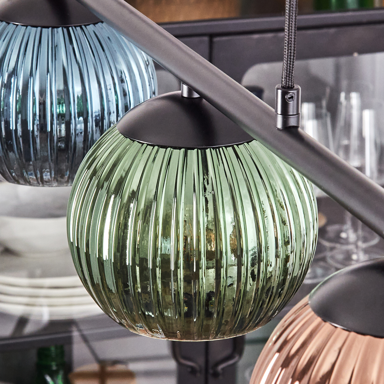 Nahaufnahme einer modernen Leuchte mit drei kugelförmigen, geriffelten Glasschirmen in Blau, Grün und Kupferfarben.