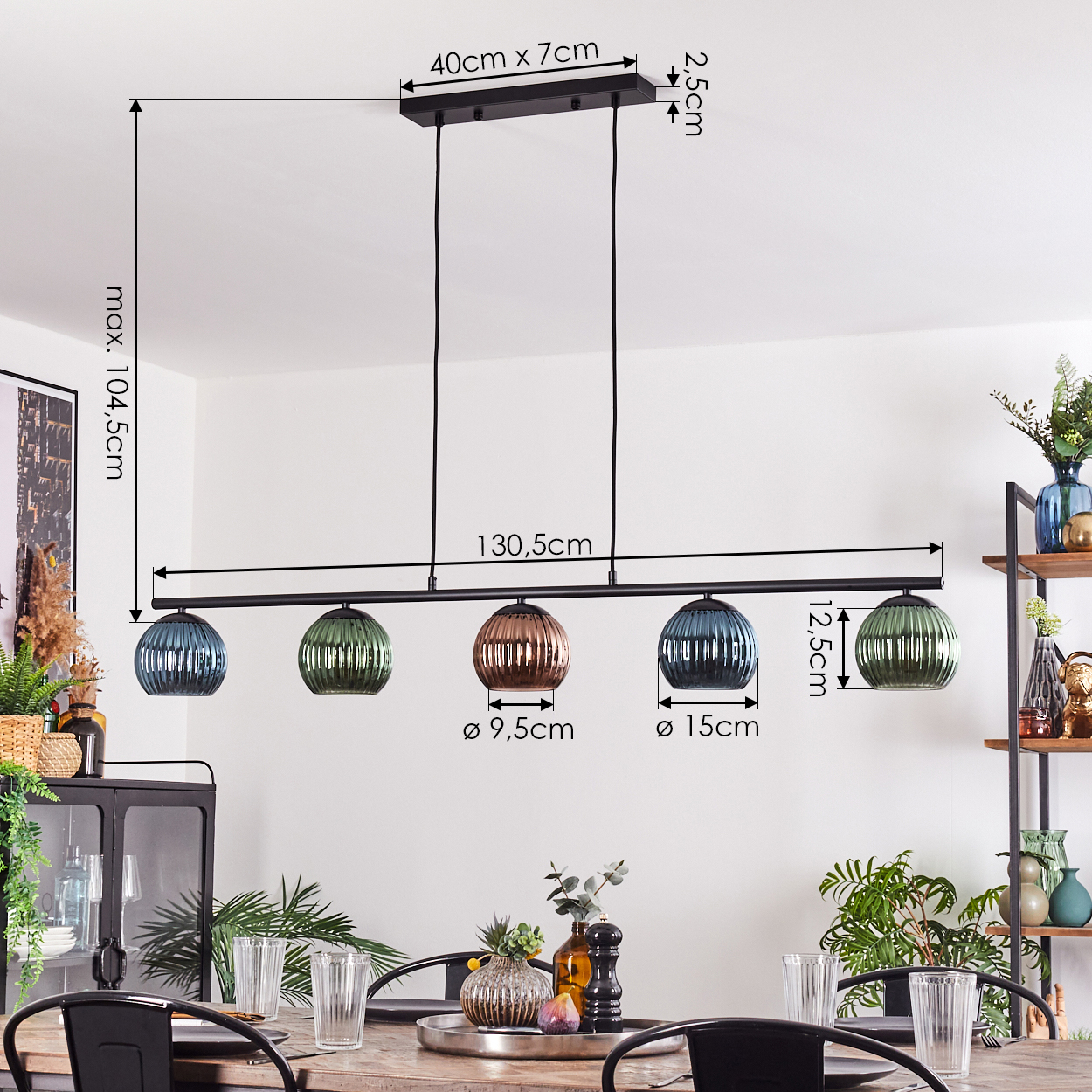 Ein modernes Esszimmer mit einem schwarzen Kronleuchter mit fünf bunten Glaslampen. Ein Tisch ist mit Gläsern und Pflanzen gedeckt.