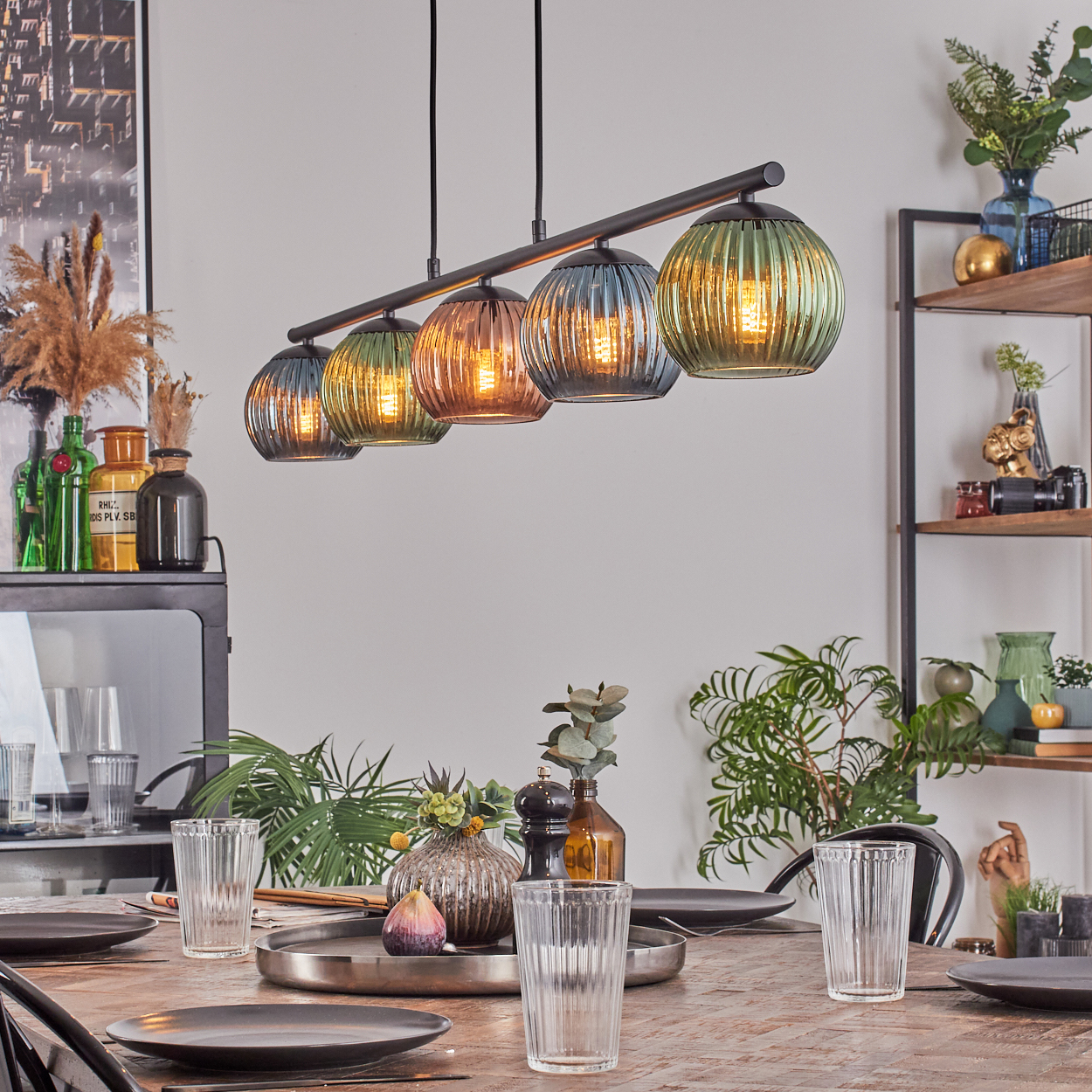 Ein Esszimmer. Ein Holztisch ist mit Tellern, Gläsern und Dekorationen gedeckt. Darüber hängt eine mehrfarbige Pendelleuchte.