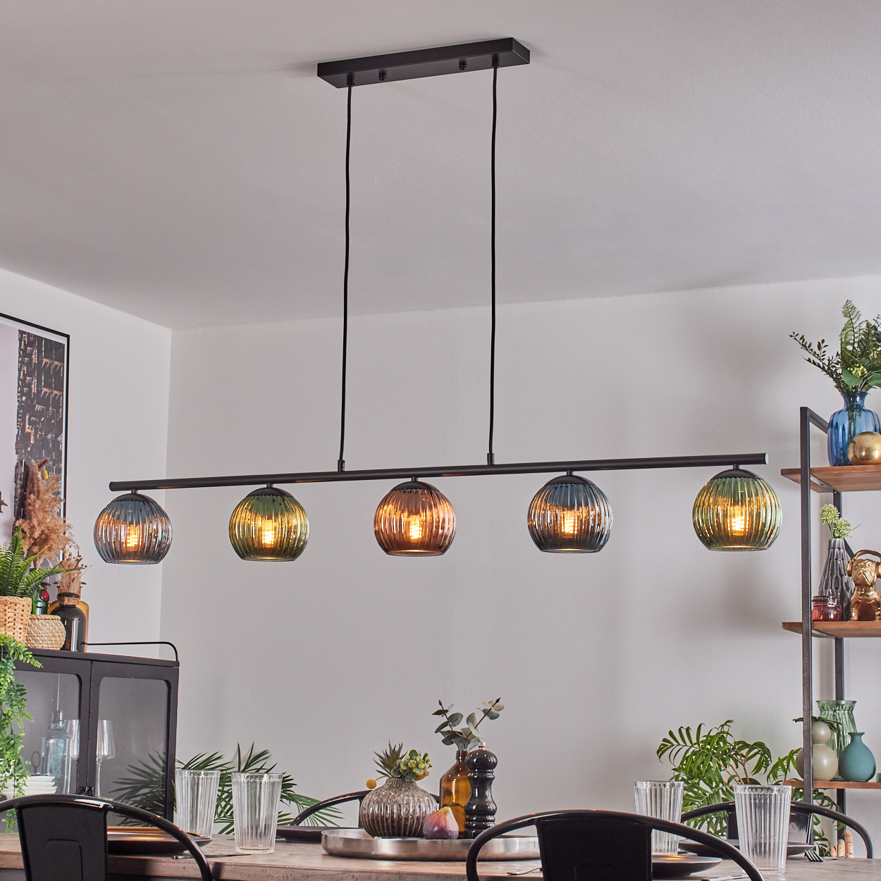 Esszimmer mit moderner Leuchte. Fünf Glaskugellampen hängen über einem Esstisch, der zum Abendessen gedeckt ist. Pflanzen und Dekoration sind sichtbar.