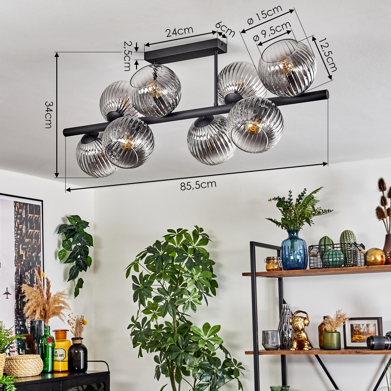 Eine moderne Deckenlampe mit Glaskugeln ist installiert. Pflanzen und Regale mit Dekoration befinden sich im Hintergrund.