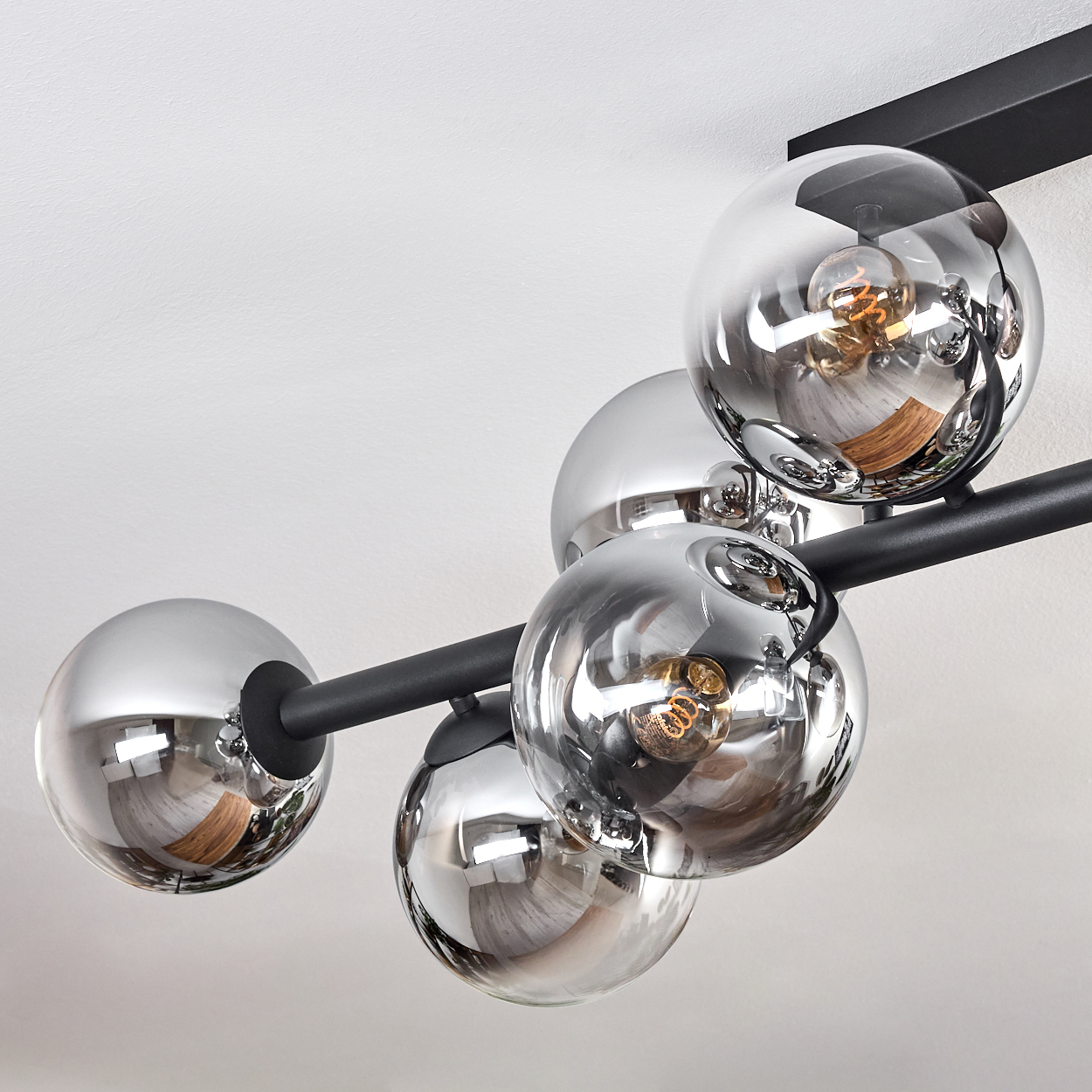 Eine moderne Deckenleuchte mit fünf Chromkugeln. Jede Kugel reflektiert den Raum und enthält eine Glühbirne. Schwarze Metallarme verbinden sie.