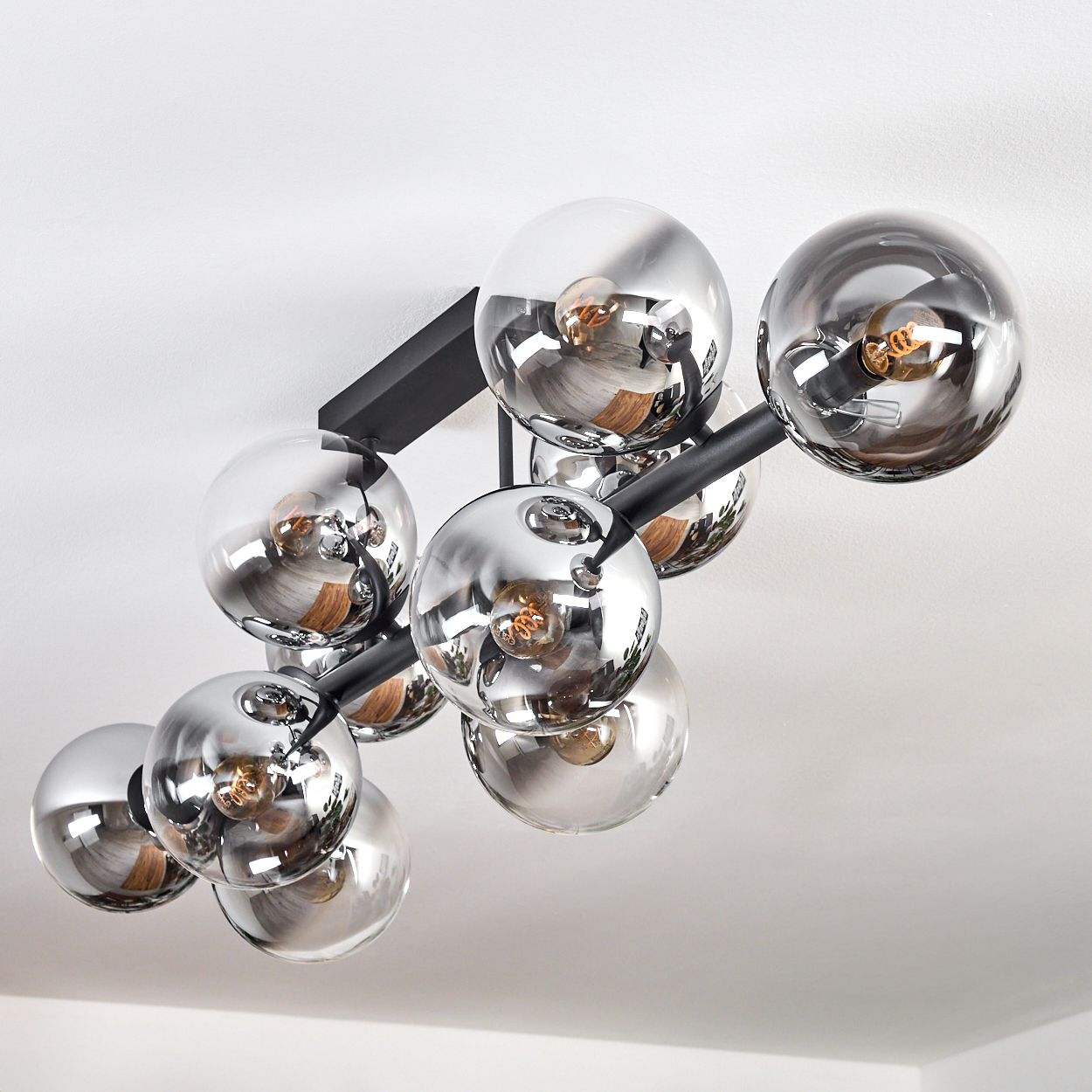 Eine moderne Deckenleuchte mit mehreren kugelförmigen Glasschirmen. Die Schirme sind reflektierend, das Gestell ist schwarz. Die Decke ist weiß.