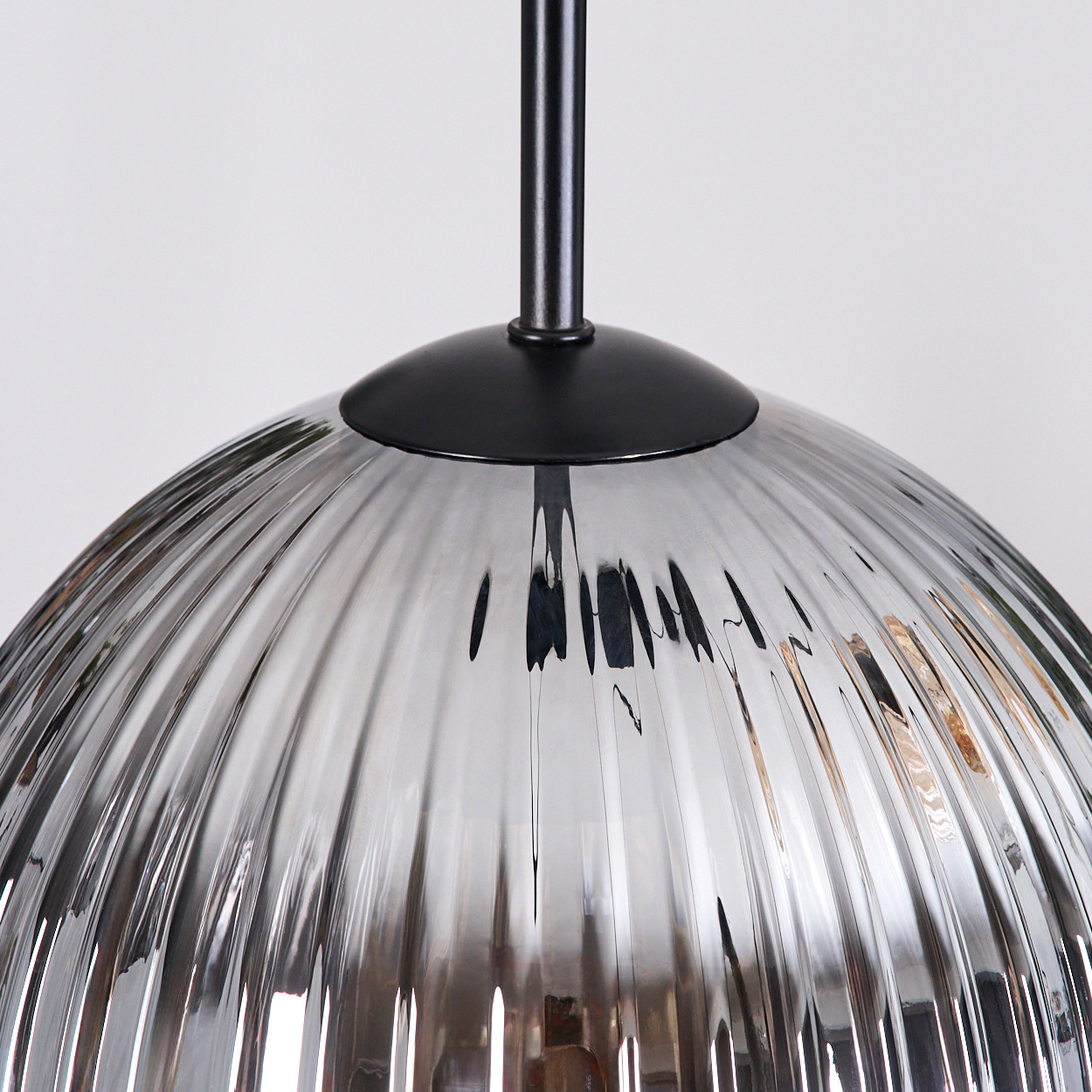 Nahaufnahme einer Glas-Pendelleuchte. Die Lampe hat einen gerippten, kuppelförmigen Schirm in Silber. Ein schwarzer Stiel und Baldachin sind sichtbar.