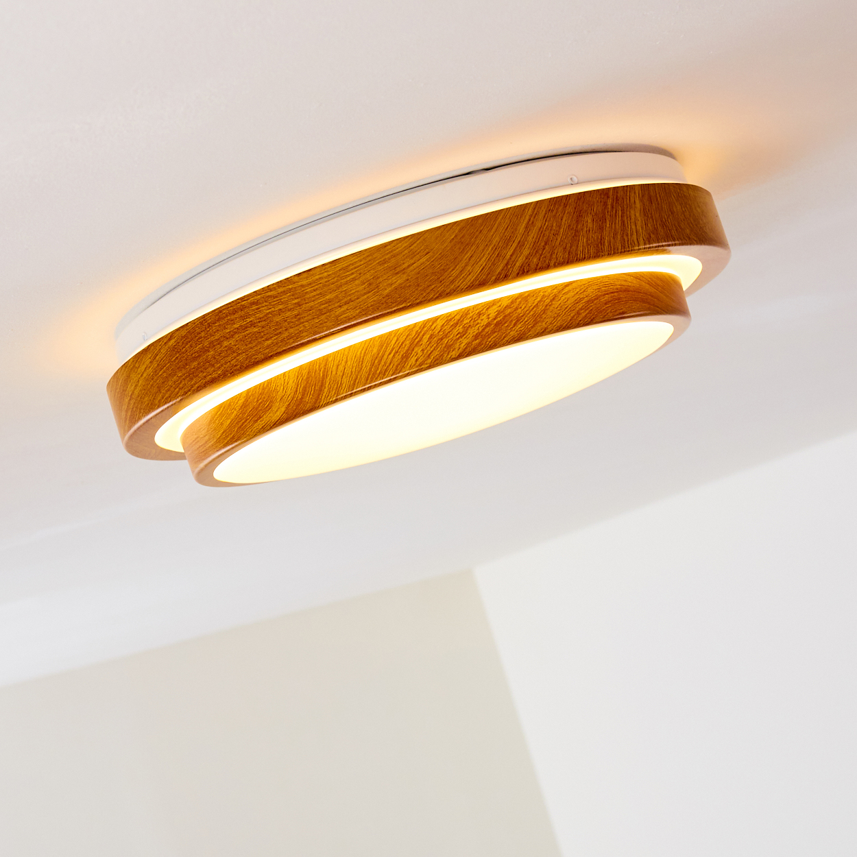 Eine moderne, geschichtete Deckenleuchte. Sie hat Holzringe und strahlt ein warmes Licht aus. Der Hintergrund ist eine weiße Decke.