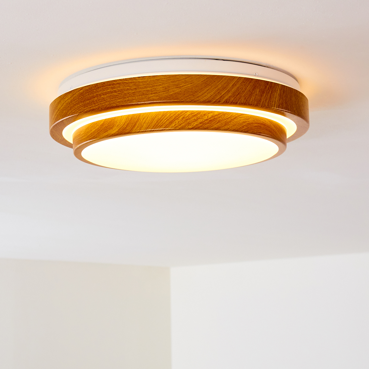 Eine moderne Deckenleuchte. Sie hat Holz- und weiße Kreisschichten und strahlt warmes Licht aus. Der Hintergrund ist eine weiße Decke.