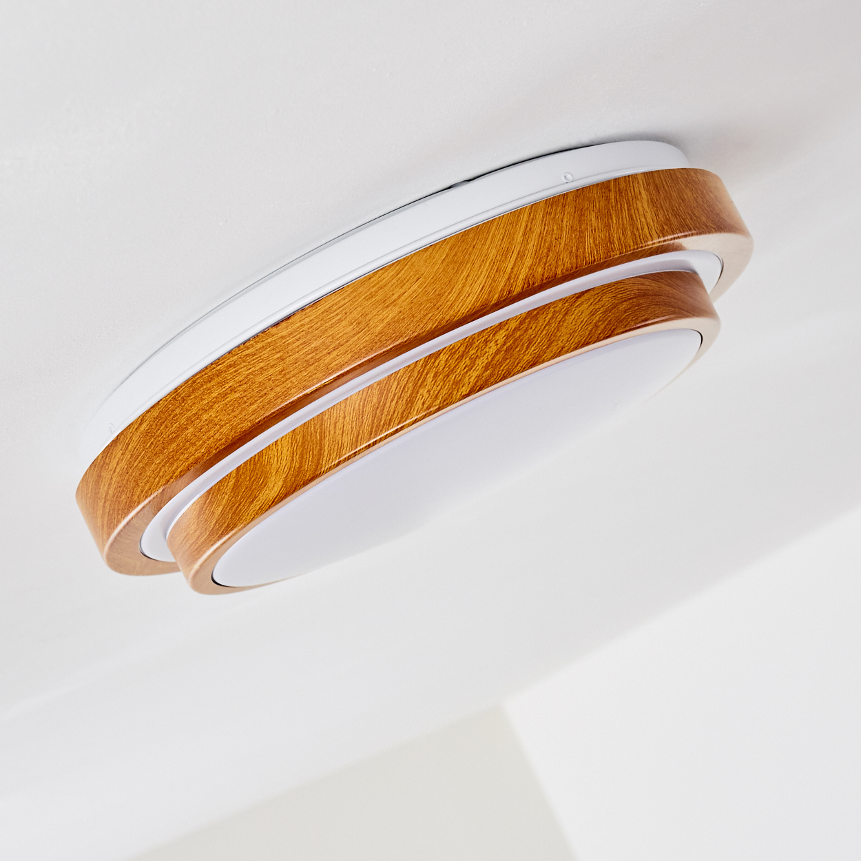 Eine moderne Deckenleuchte. Sie hat eine Holzoptik mit weißen Akzenten und ein helles, kreisförmiges Licht in der Mitte.