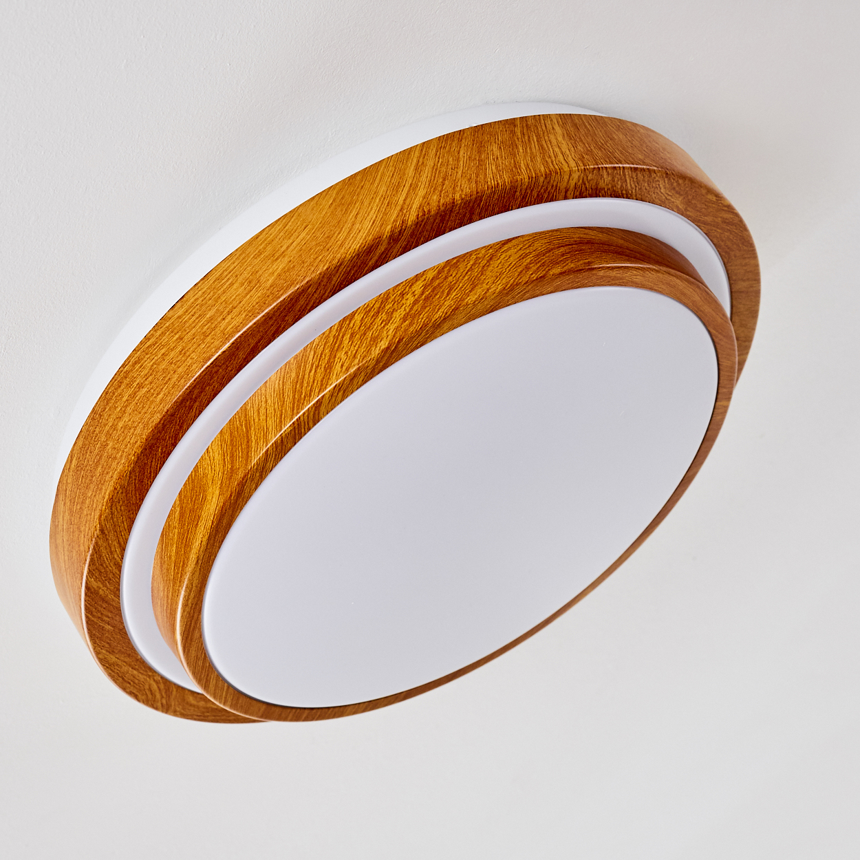 Eine moderne Deckenleuchte mit Holzrahmen und weißem Kunststoff-Innenraum. Die Leuchte ist oval und an einer weißen Decke montiert.