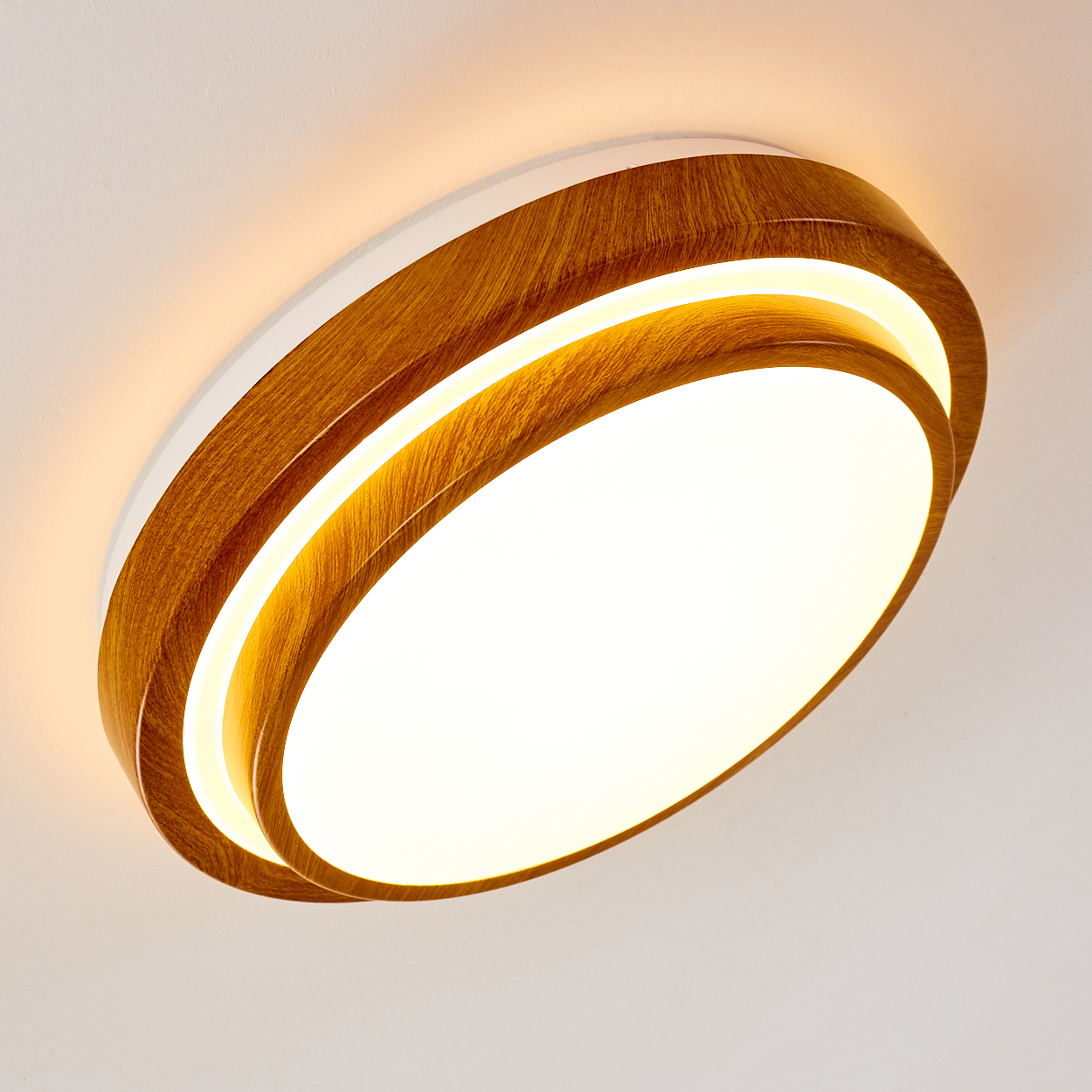 Eine moderne Deckenleuchte mit Holzrahmen und weißem Innenring. Das Licht ist an, mit hellem Weiß und warmem gelbem Licht.