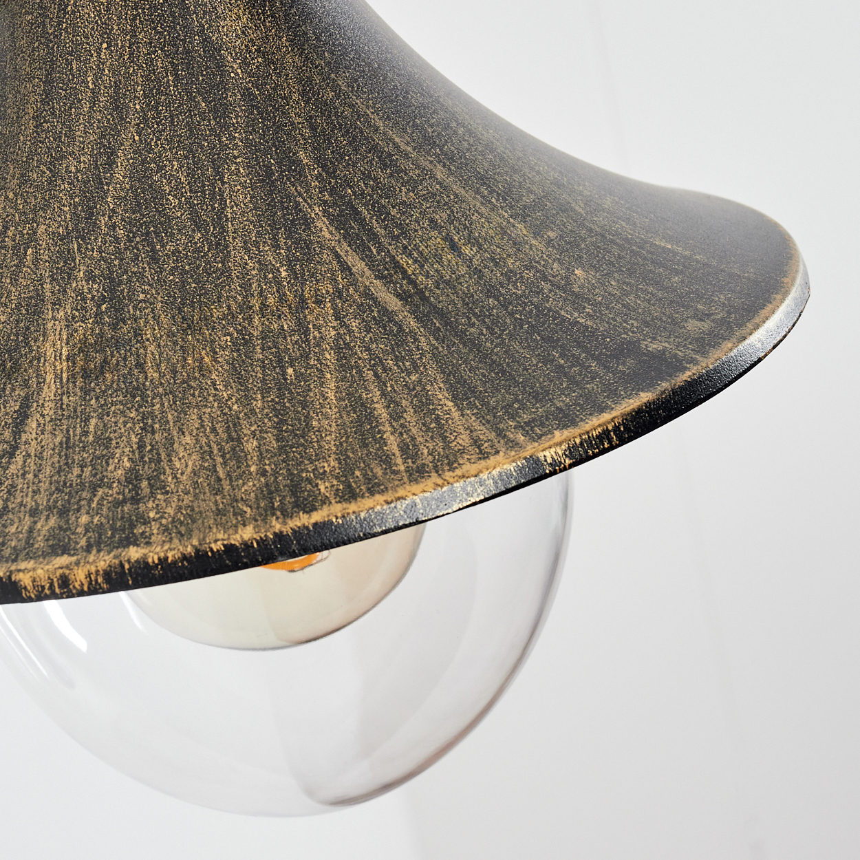 Nahaufnahme einer Hängelampe. Die Lampe hat einen schwarz-goldenen Schirm und eine transparente Glaskugel. Der Hintergrund ist weiß.