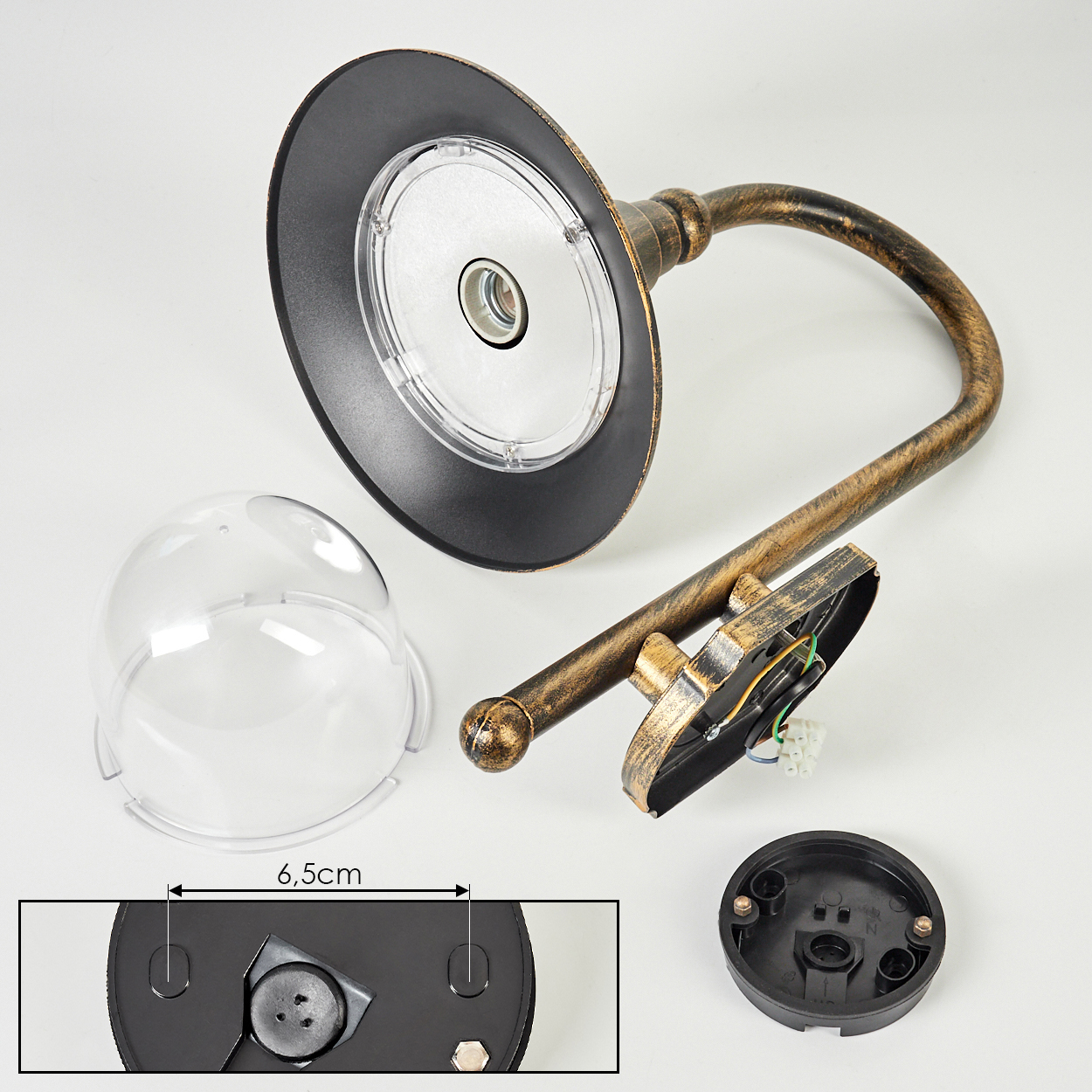 Eine zerlegte Außenlampe mit klarer Kuppel, schwarzen und goldenen Metallteilen und einem Sockel. Die Lampe liegt auf einer weißen Oberfläche.