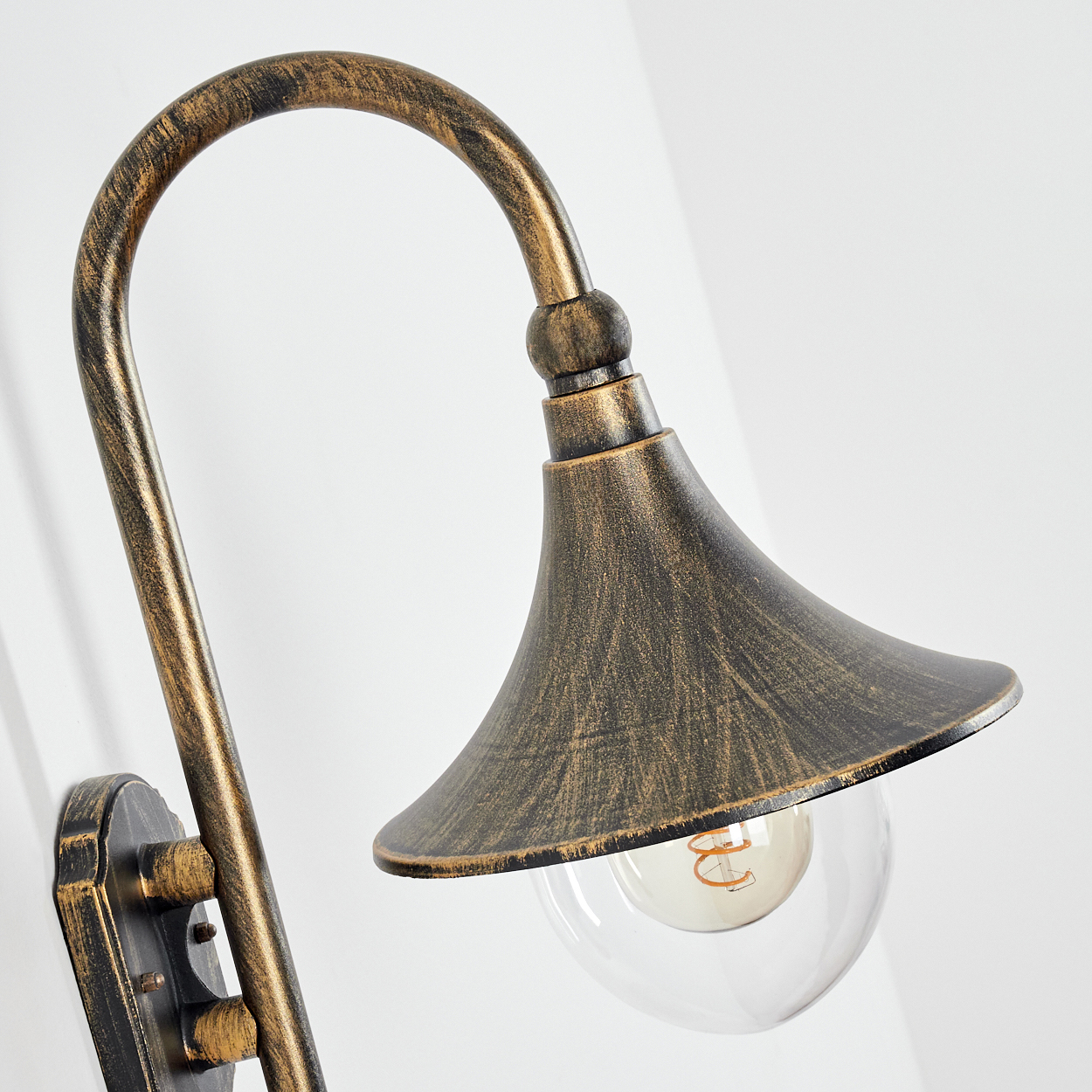 Eine dekorative Wandleuchte mit gebogenem Arm und glockenförmigem Schirm. Die Lampe hat eine klare Glühbirne und eine goldene Vintage-Oberfläche.