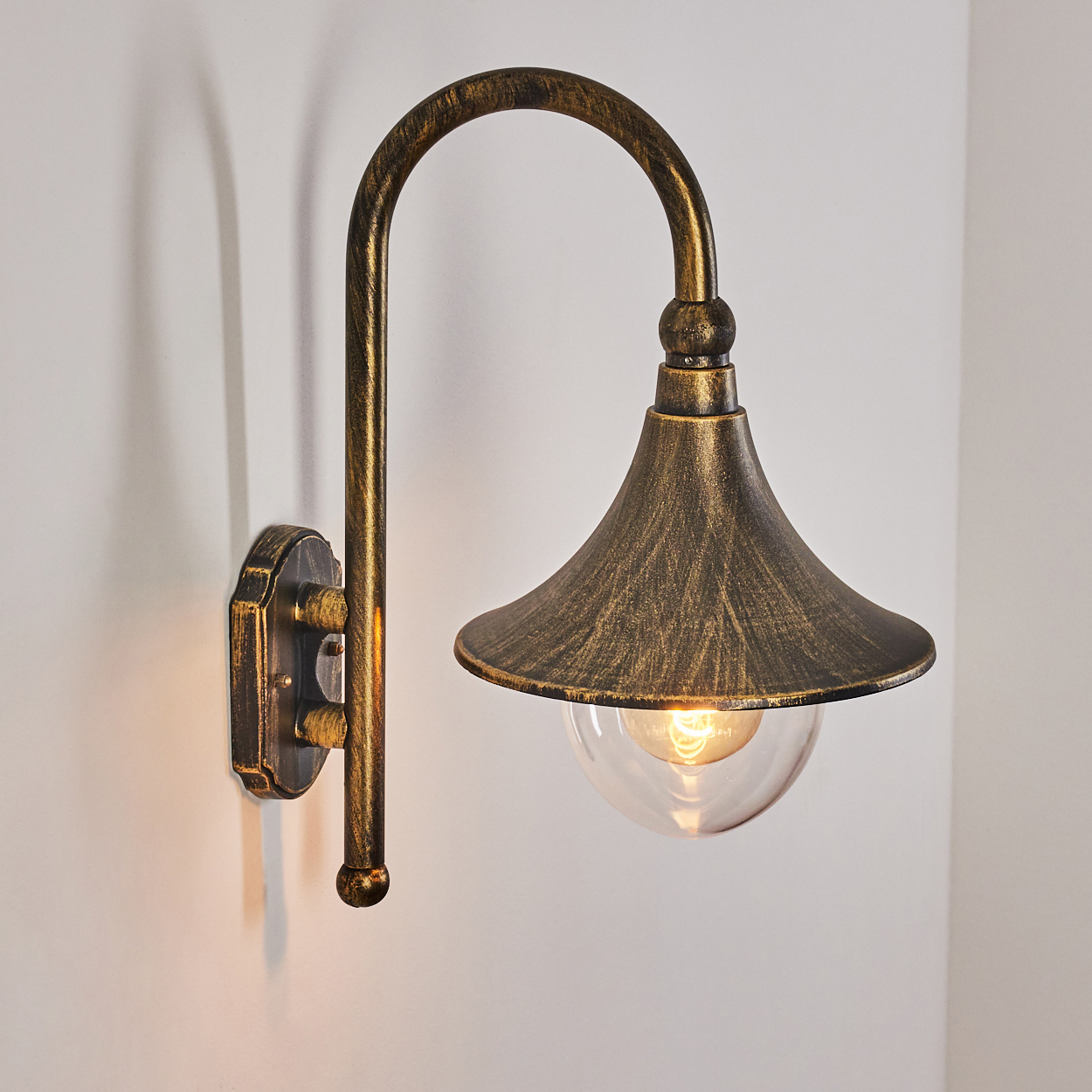 Eine antike Wandlampe mit gebogenem Arm und glockenförmigem Schirm, mit klarem Glaskugel, an einer weißen Wand montiert.