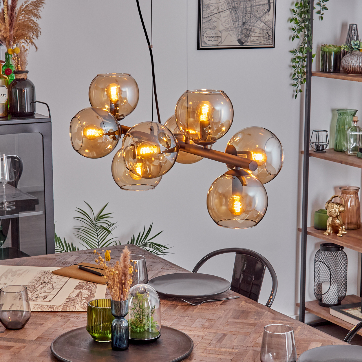 Ein Esszimmer mit Holztisch. Eine stilvolle Hängelampe hängt darüber. Verschiedene Dekorationsartikel befinden sich auf dem Tisch und in Regalen.