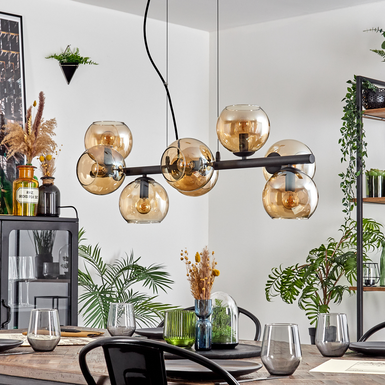Esszimmer mit Holztisch, Gläsern und schwarzer Leuchte mit bernsteinfarbenen Glaskugeln.