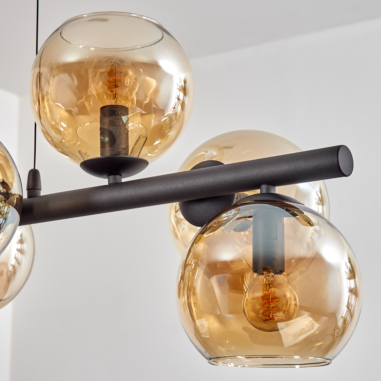 Nahaufnahme eines modernen Kronleuchters. Er hat mehrere bernsteinfarbene Glaskugeln mit sichtbaren Glühbirnen und einen schwarzen Metallrahmen.