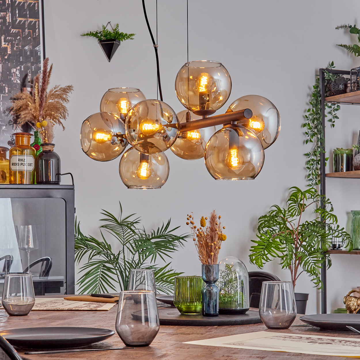 Esszimmer mit Holztisch, Gläsern, Tellern und Kronleuchter mit Glaskugeln. Pflanzen und Dekorationen sind sichtbar.
