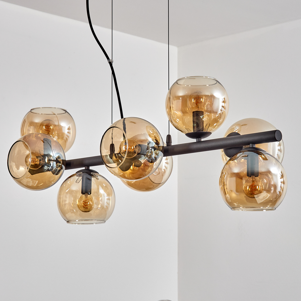 Eine moderne Deckenleuchte mit mehreren kugelförmigen Glasschirmen in Bernsteinfarbe, die von der Decke hängt, vor einer weißen Wand.