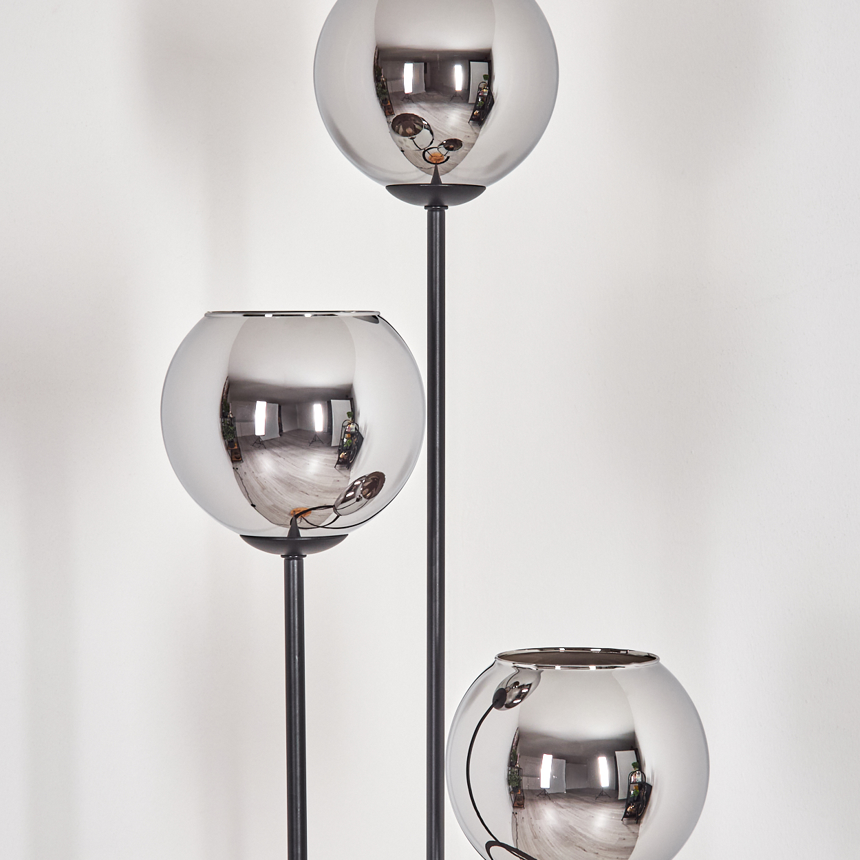 Drei verspiegelte Glaskugellampen auf schwarzen Stielen vor einer weißen Wand. Die Kugeln reflektieren den Raum und die Beleuchtung.