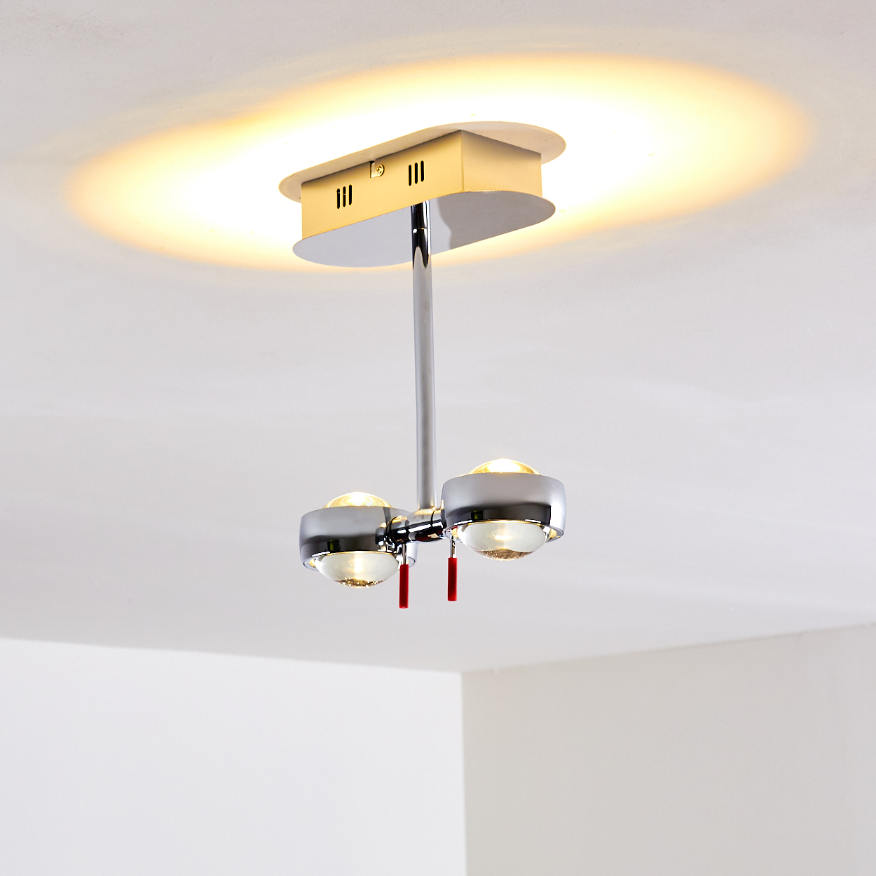 Eine moderne Deckenlampe mit zwei Lichtern. Chrom- und Silberarmatur mit roten Akzenten. Die Decke ist weiß mit warmem Licht.