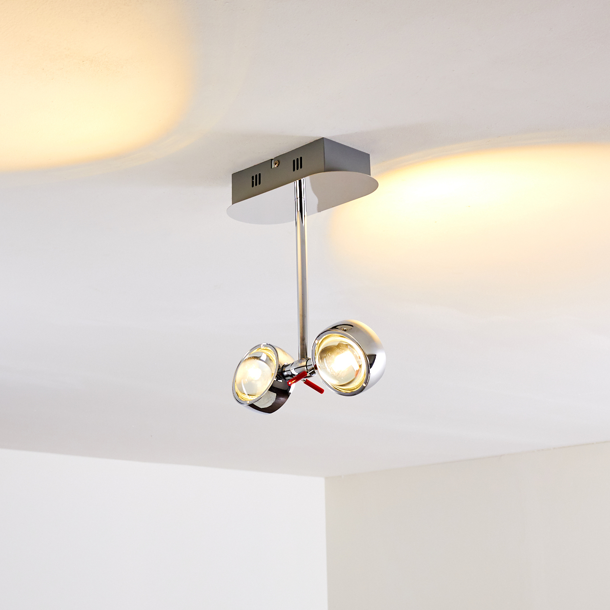 Eine moderne Deckenleuchte mit zwei Chrom-Strahlern. Sie ist an einer weißen Decke mit Lichtreflexion befestigt.