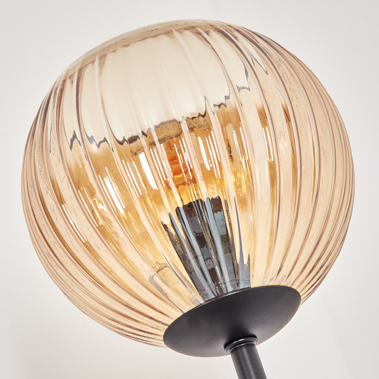 Nahaufnahme einer dekorativen Lampe. Sie hat einen gerippten, bernsteinfarbenen Glasschirm und einen schwarzen Sockel.