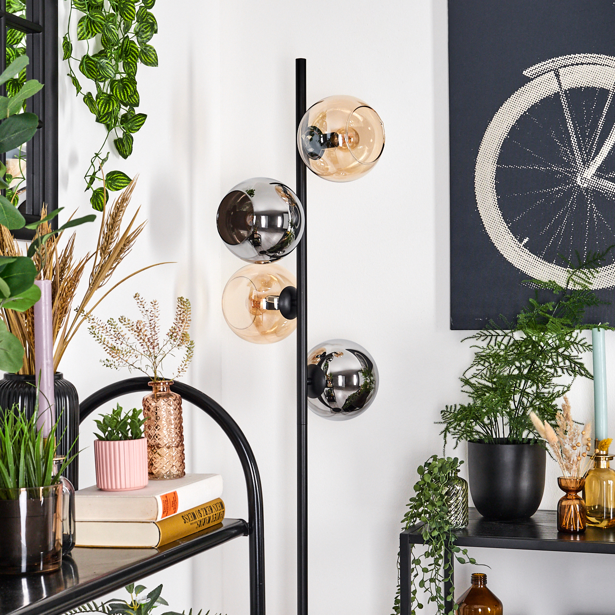 Ein modernes Interieur mit einer schwarzen Stehlampe mit Glaskugeln, Pflanzen, einem schwarzen Regal mit Büchern und einem Fahrradrad-Kunstwerk.