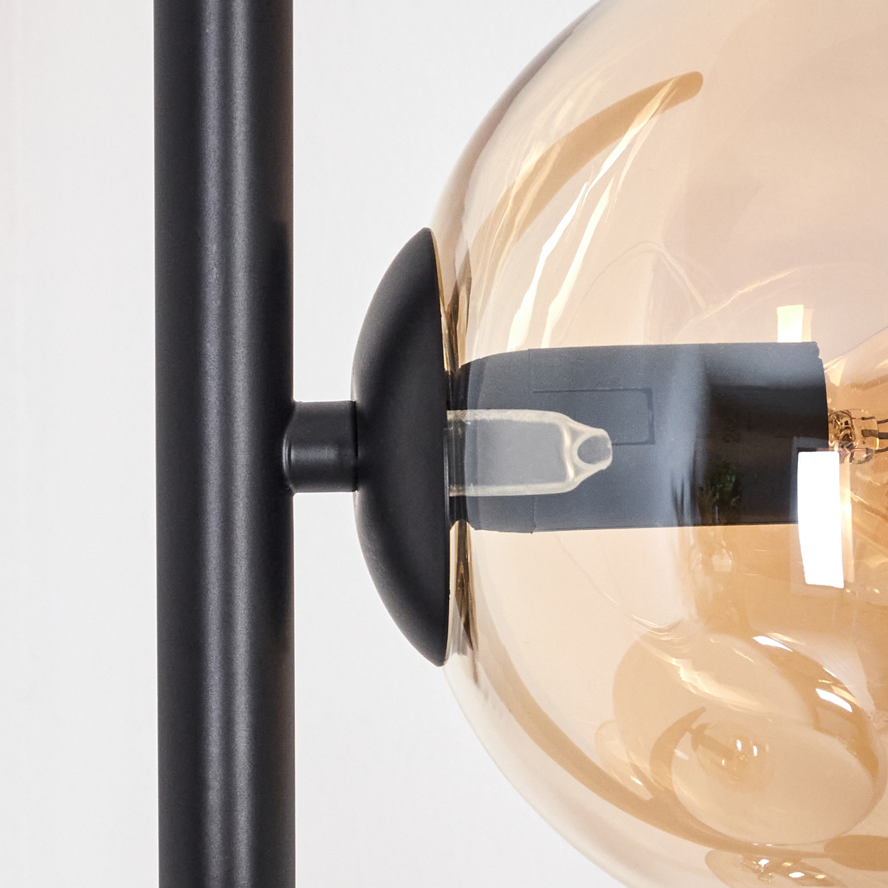 Nahaufnahme einer Lampe. Eine schwarze Metallstange trägt einen kugelförmigen, bernsteinfarbenen Glasschirm. Die Glühbirne ist sichtbar.