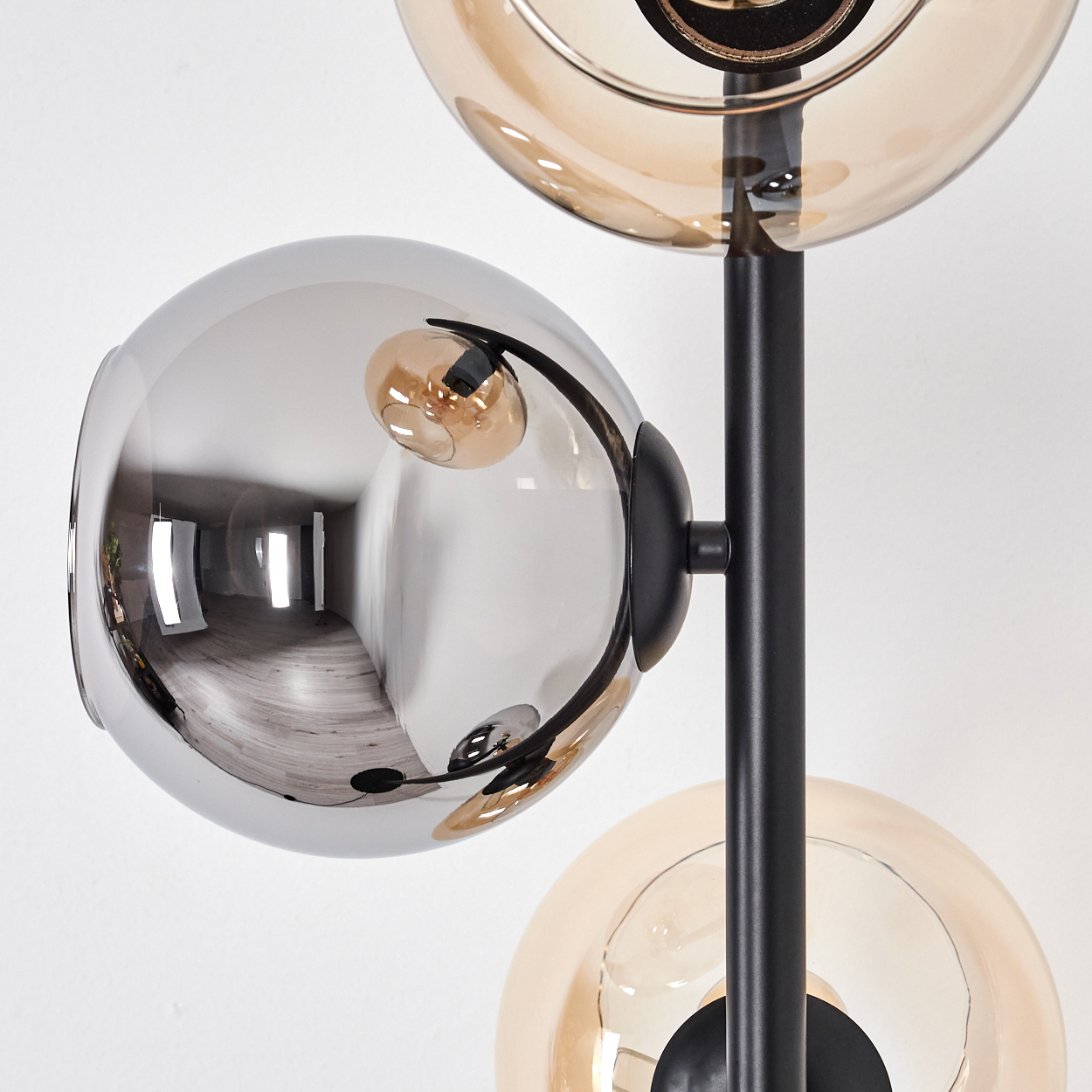 Nahaufnahme einer modernen Lampe mit drei kugelförmigen Schirmen: grau, klar und gold. Schwarzer Stiel und weißer Hintergrund.