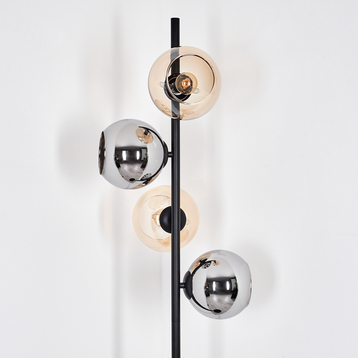 Eine moderne Stehlampe. Sie hat einen schwarzen Pfahl mit kugelförmigen Leuchten. Einige sind verchromt, andere bernsteinfarbenes Glas.
