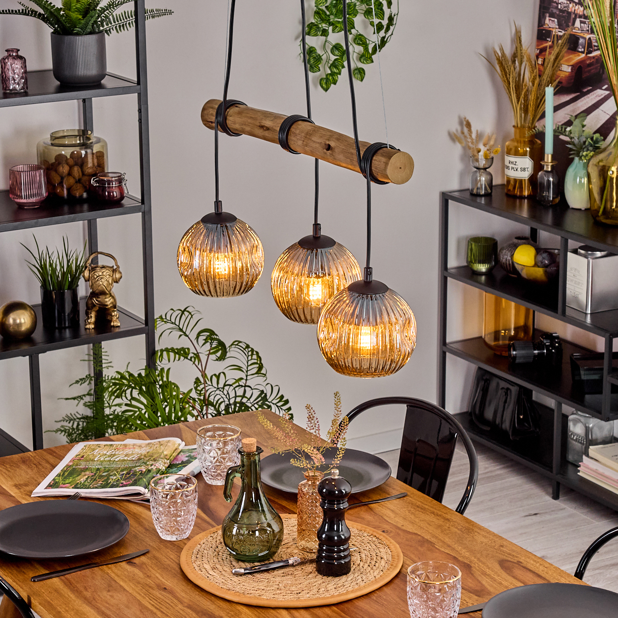 Esszimmer mit Holztisch, drei Hängelampen und Dekorationsartikeln auf Regalen. Tisch zum Abendessen gedeckt.
