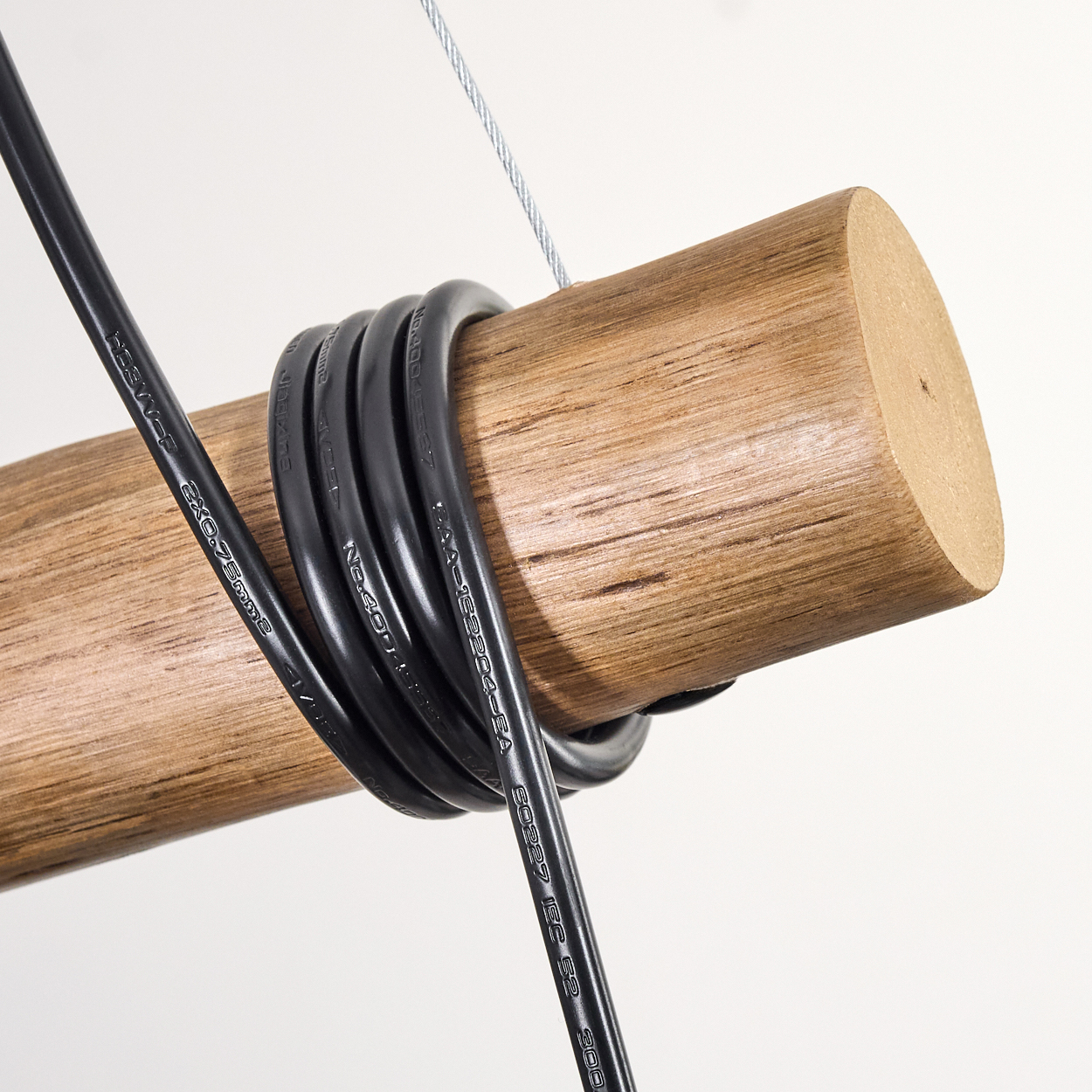 Nahaufnahme eines Holz-Zylinders mit schwarzen Kabeln. Ein silberner Draht hängt von oben. Der Hintergrund ist weiß.