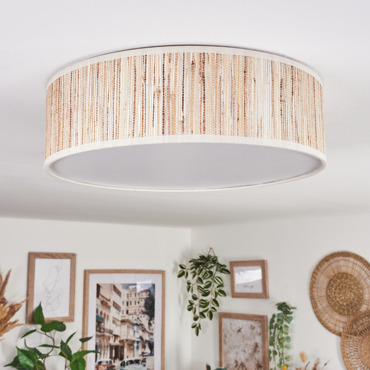 Ein gewebter Lampenschirm hängt von der Decke. Darunter dekorieren gerahmte Bilder und Pflanzen die Wand, mit einer Wanddekoration.
